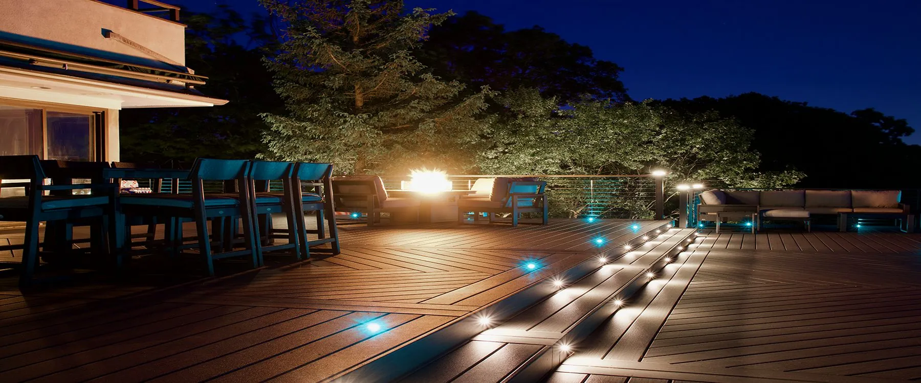 Luxury Trex deck at night with teal LED riser lighting and a fire feature — Pinnacle Decking Hudson Valley NY